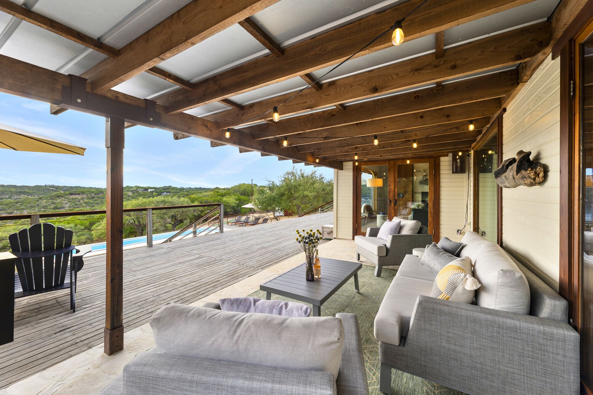 Un área de estar al aire libre techada, con piscina, terraza de madera y vistas del paisaje.