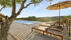 Une terrasse en bois avec une piscine, des chaises longues et un parasol.