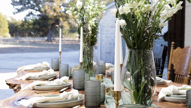 Une table dressée pour le repas, avec des assiettes, des couverts et des vases décoratifs ornés de fleurs.