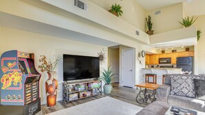 A spacious living room with a large flat-screen TV, arcade games, and a cozy seating area. - Resort Pool & Spa Access: Mesquite Condo! (Mesquite)