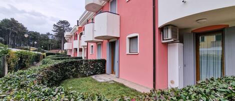 A row of pink and white buildings with balconies, surrounded by well-maintained greenery.