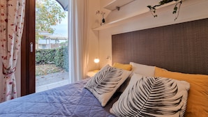 Una camera da letto con un letto, cuscini, un comodino, una lampada e una finestra con tende.