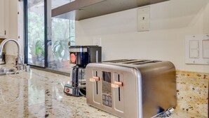 A kitchen with a toaster, a coffee maker, and a window with a view of greenery. - Serene Poway Home w/ Private Pool: Pet Friendly! (Poway)