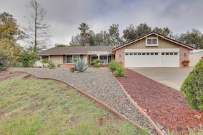 A single-story house with a garage, surrounded by a landscaped garden with gravel and mulch paths, and various plants.