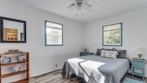 A bedroom with a bed, two nightstands, a wooden shelf with decorative items, a ceiling fan, and two windows with blinds. - Lovely Smoky Mountain Cottage w/ Deck + Views! (Topton)