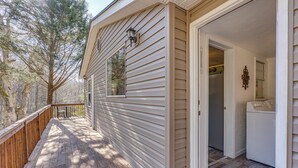 A wooden deck with a view of trees, a door leading to a laundry room, and a small window with a light fixture. - Lovely Smoky Mountain Cottage w/ Deck + Views! (Topton)