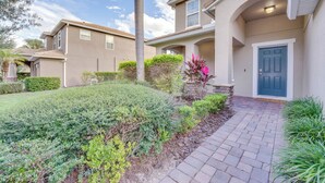 A residential building with a paved driveway, a blue door, and landscaped garden areas. - ~ 6 Mi to Disney: Kissimmee Vacation Villa w/ Pool (Kissimmee)