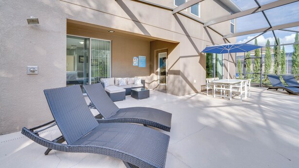 A covered outdoor area with lounge chairs, a table, and a blue umbrella. - ~ 6 Mi to Disney: Kissimmee Vacation Villa w/ Pool (Kissimmee)