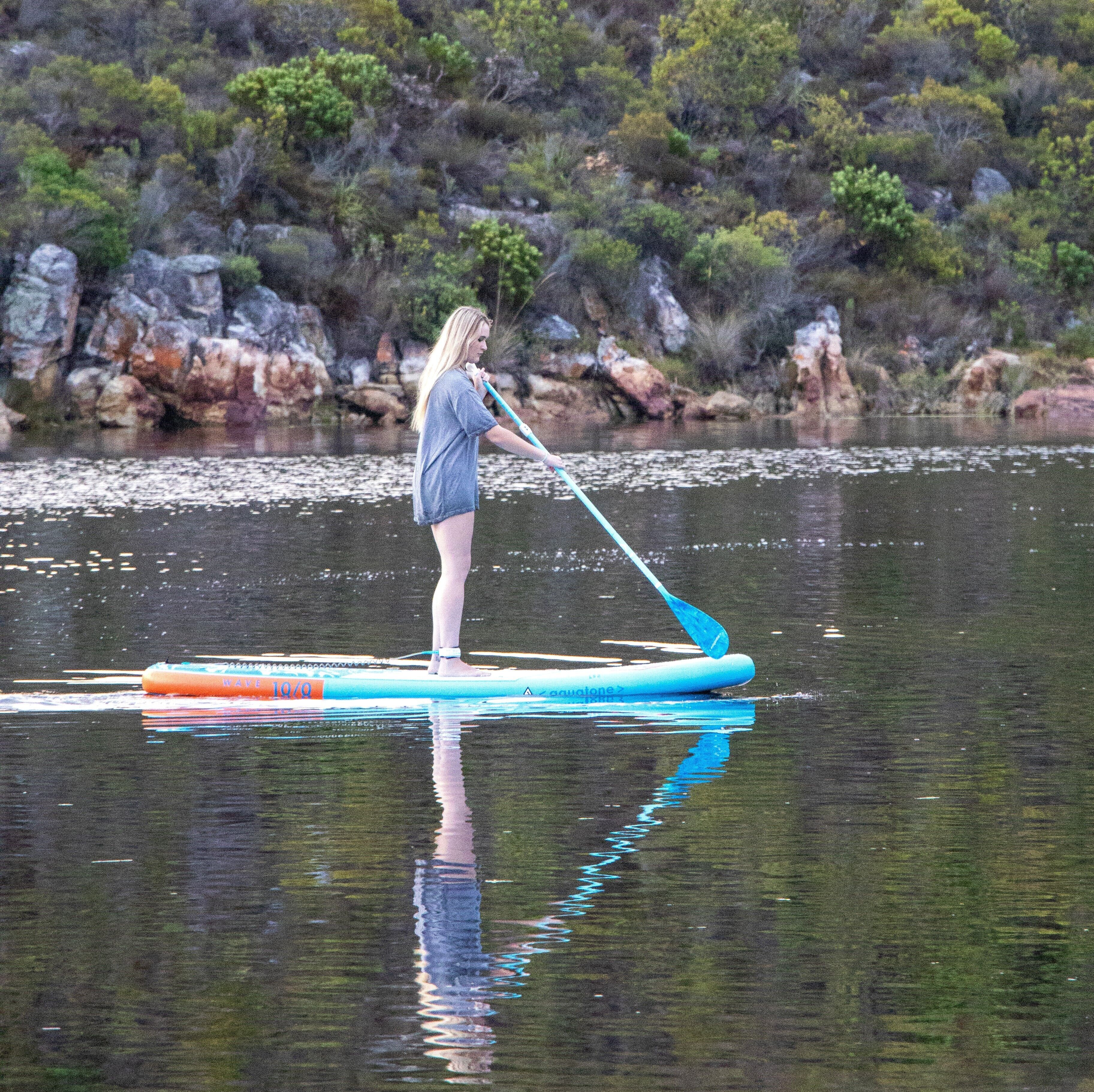Une personne pratiquant le stand-up paddle sur une étendue d'eau calme, avec un paysage naturel en arrière-plan.