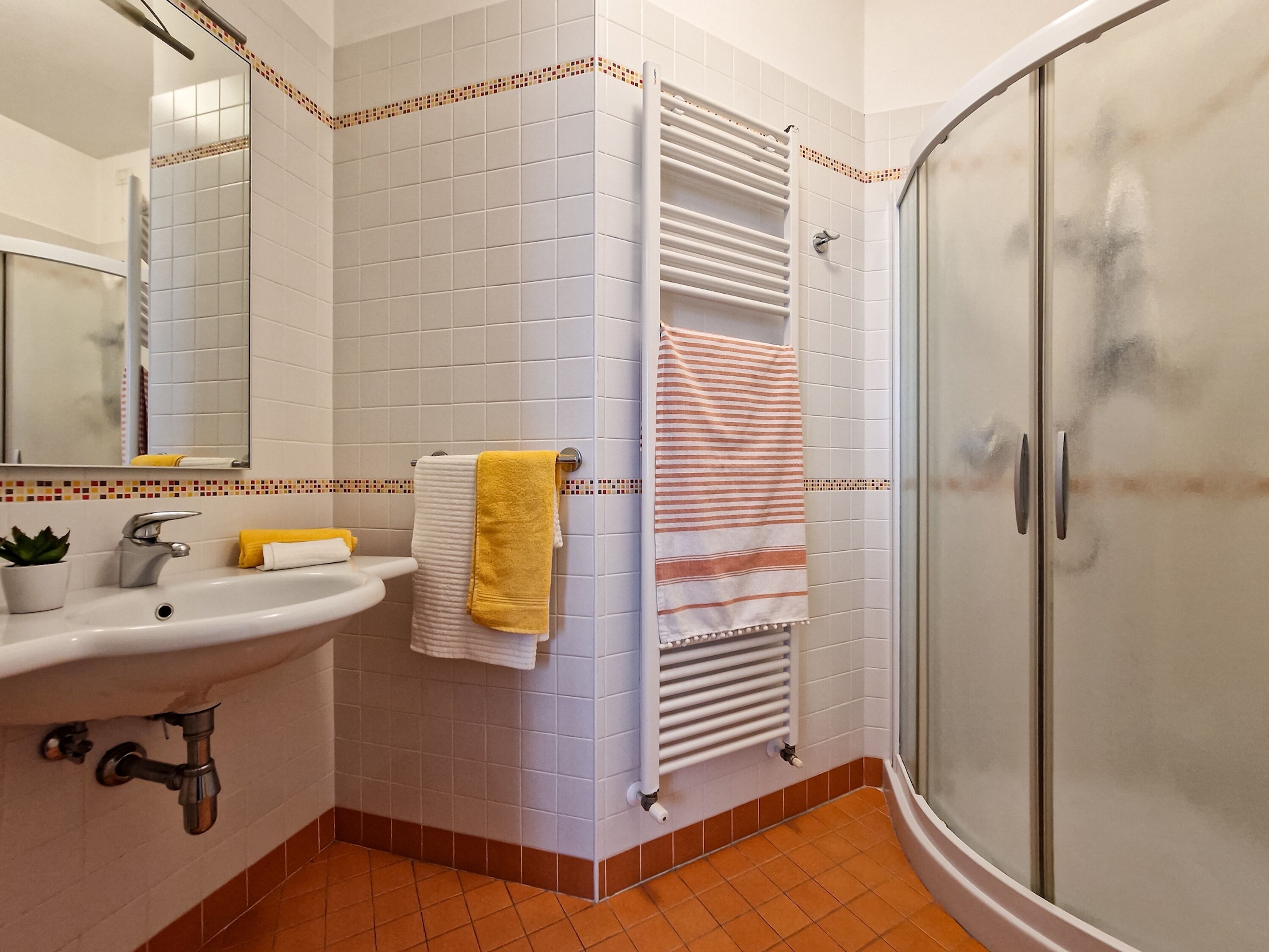 Une salle de bain équipée d’un lavabo, d’un miroir, d’un porte-serviettes, d’une douche et de murs carrelés.