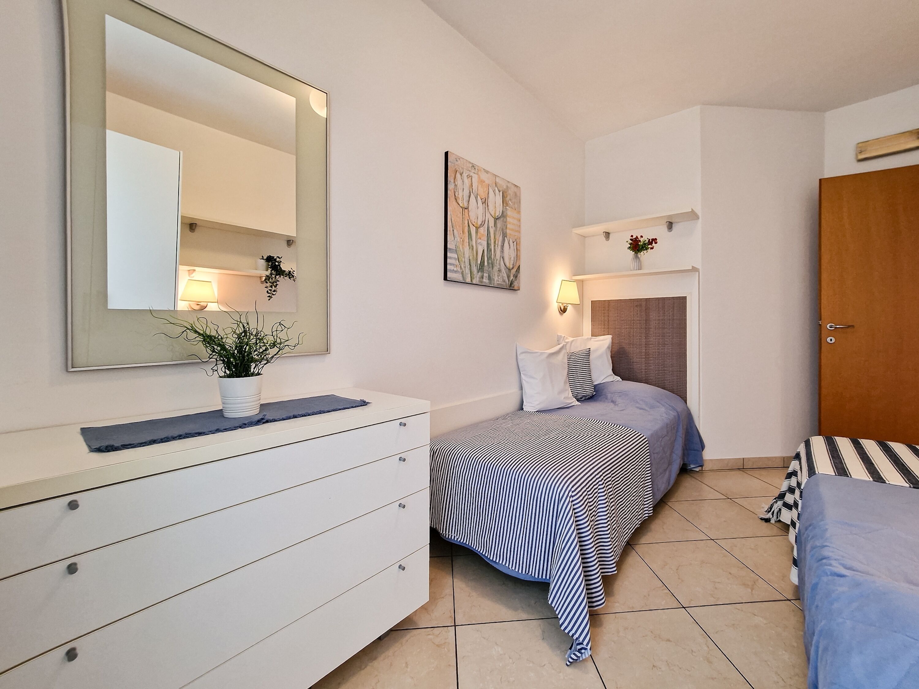 A bedroom with a bed, a dresser, a mirror, a painting, and a door.