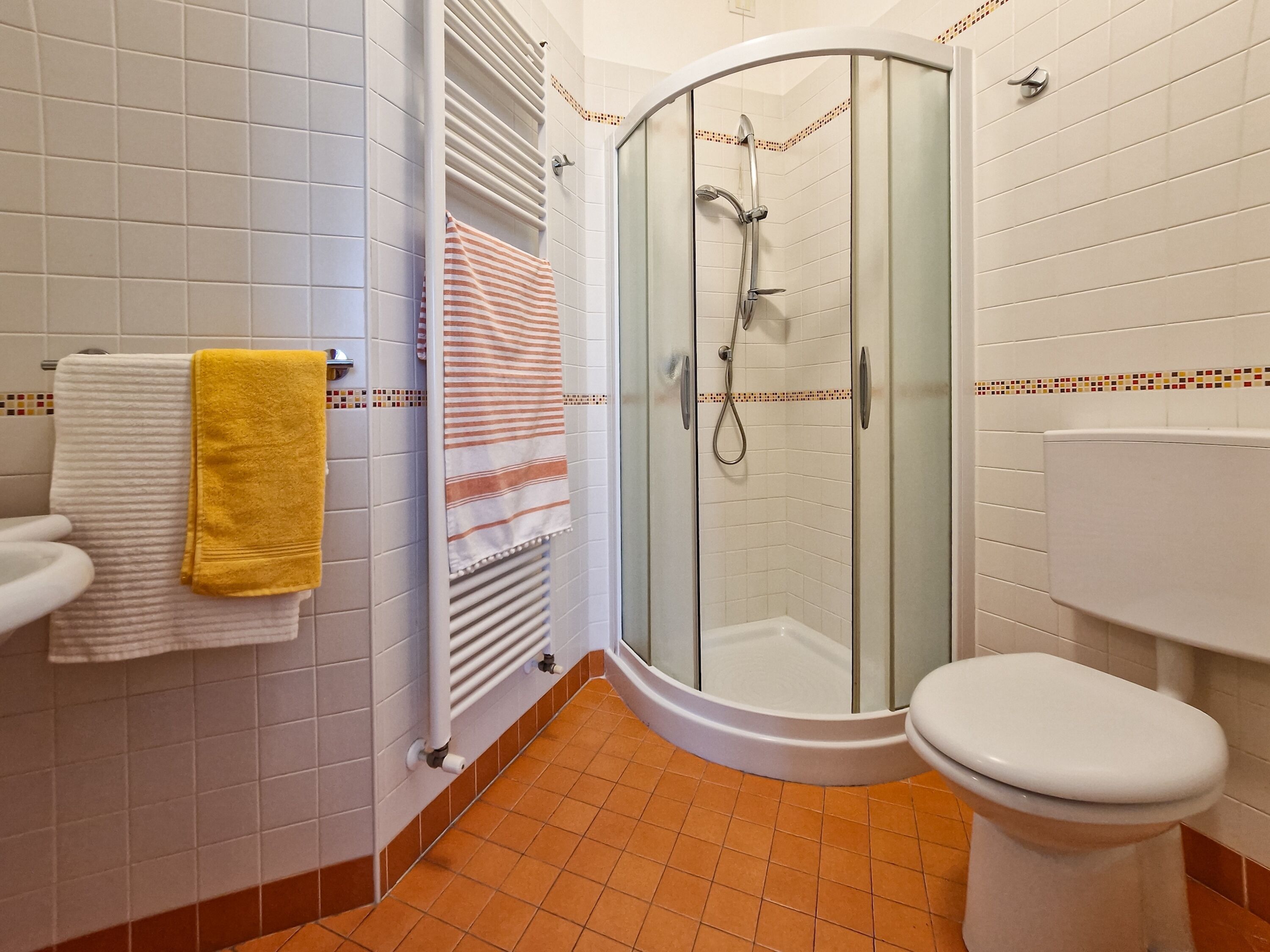 A bathroom with a glass-enclosed shower, a toilet, and a towel rack with towels.