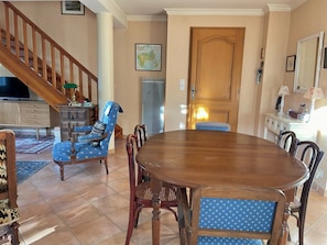 A dining area with a wooden table and chairs, a staircase, and a television in the background.