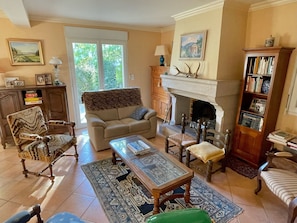 A living room with a sofa, armchairs, a fireplace, a bookshelf, and a large window.