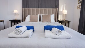 A neatly made bed with two pillows, two side tables with lamps, and a large window with curtains. - Palm Beach Sea View Apt by TrulyCyprus (Limassol)