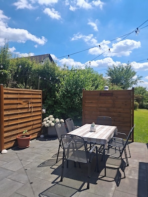 An outdoor patio with a wooden table and chairs, surrounded by a wooden fence and greenery. - Gemütliche Ferienwohnung Taube am Fuße des Stammbergs in der Fränkischen Toskana (Schammelsdorf)