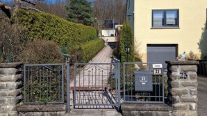 A gated entrance to a residential area with a yellow building, a mailbox marked '23', and a clear sky.