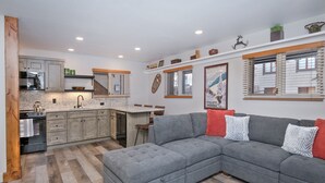 A modern kitchen with granite countertops, a built-in oven, and a dining area with a gray sectional sofa.