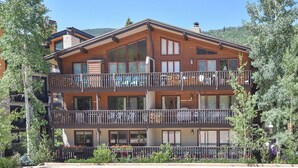 A two-story wooden building with balconies, large windows, and a mountain backdrop.
