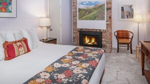A hotel room with a bed, a fireplace, a chair, and a desk.
