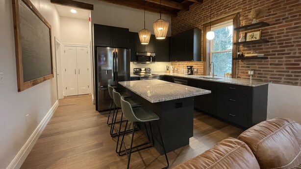 Una cocina moderna con una isla central, armarios oscuros y una pared de ladrillo decorativa.