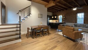 Amplia sala de estar con una escalera de madera, una mesa de comedor con sillas, un sofá y una cocina al fondo.