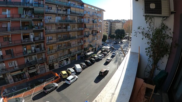 Um edifício residencial com várias andares, varandas, vista para a rua e carros estacionados.