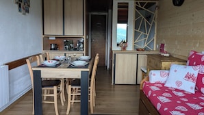 A compact living space with a dining area, kitchenette, and a cozy bed with patterned bedding. - Duplex 4/6 Pers Dans une Ambiance Chaleureuse Avec vue Imprenable sur le Sancy (Murat-le-Quaire)