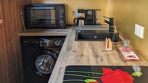 A compact kitchen with a washing machine, a microwave, a coffee maker, and a small sink. - Duplex 4/6 Pers Dans une Ambiance Chaleureuse Avec vue Imprenable sur le Sancy (Murat-le-Quaire)