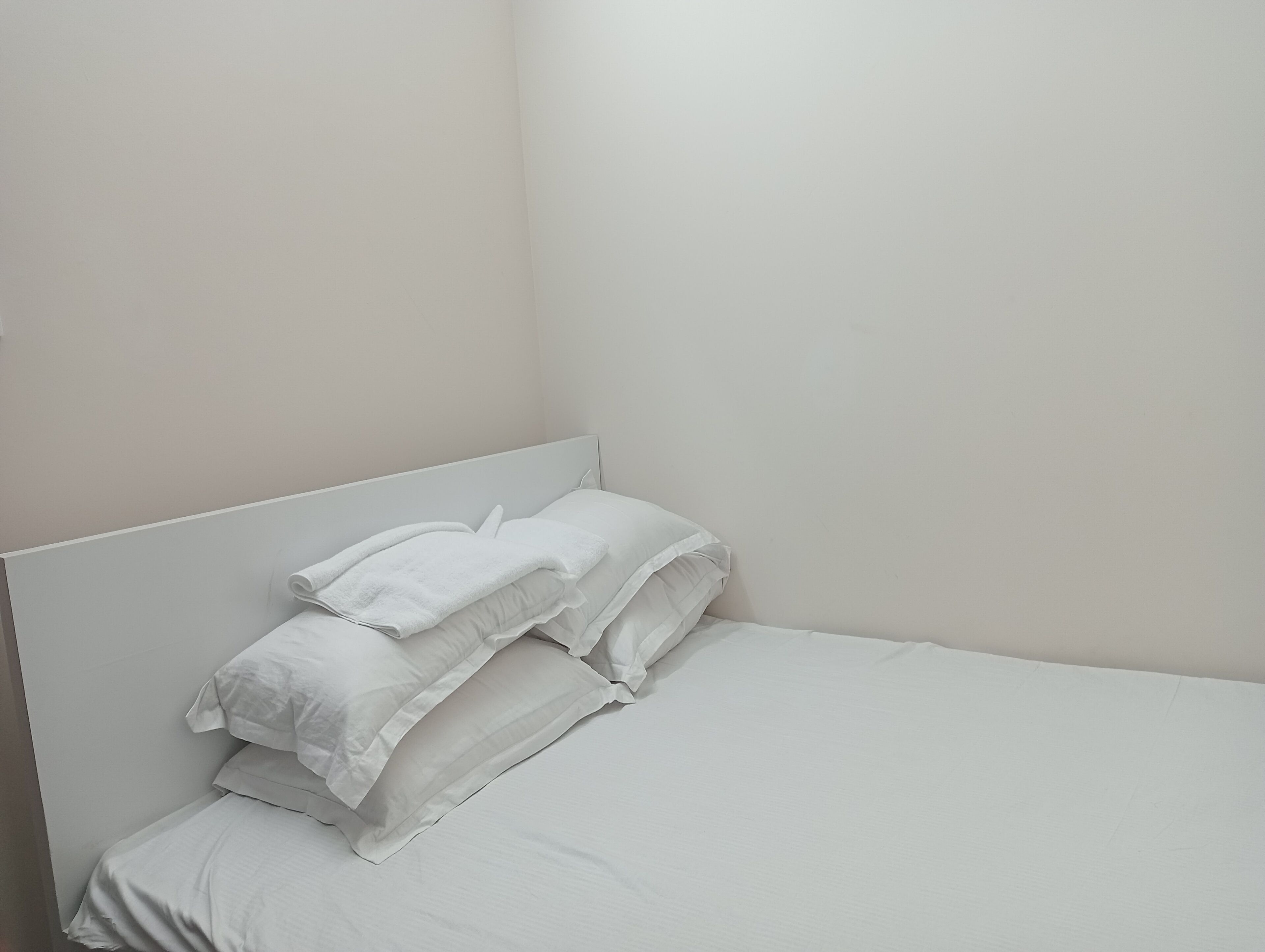 A single bed with white linens and pillows in a room with plain walls.