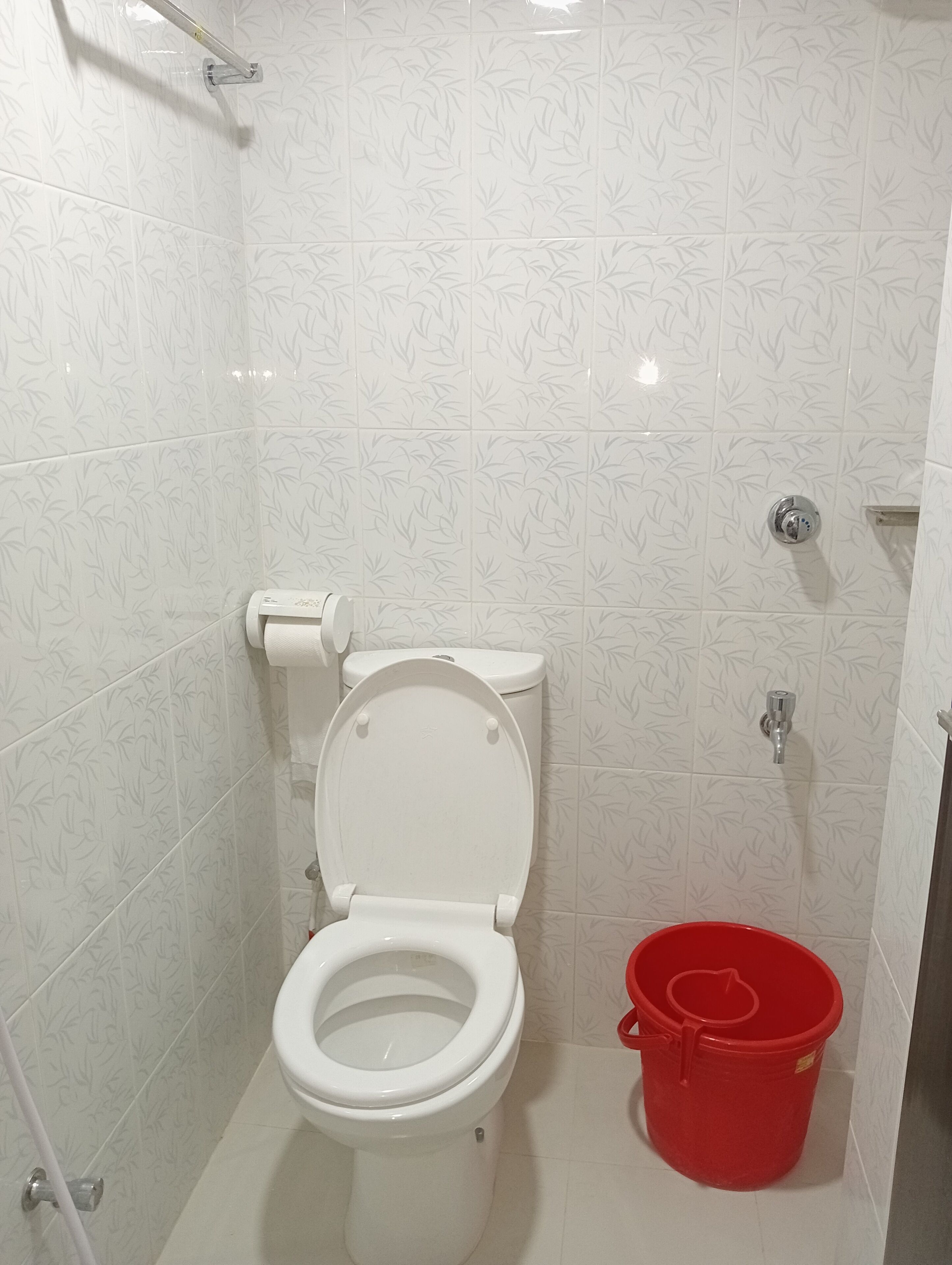 A bathroom with a toilet, a red bucket, and a shower area.