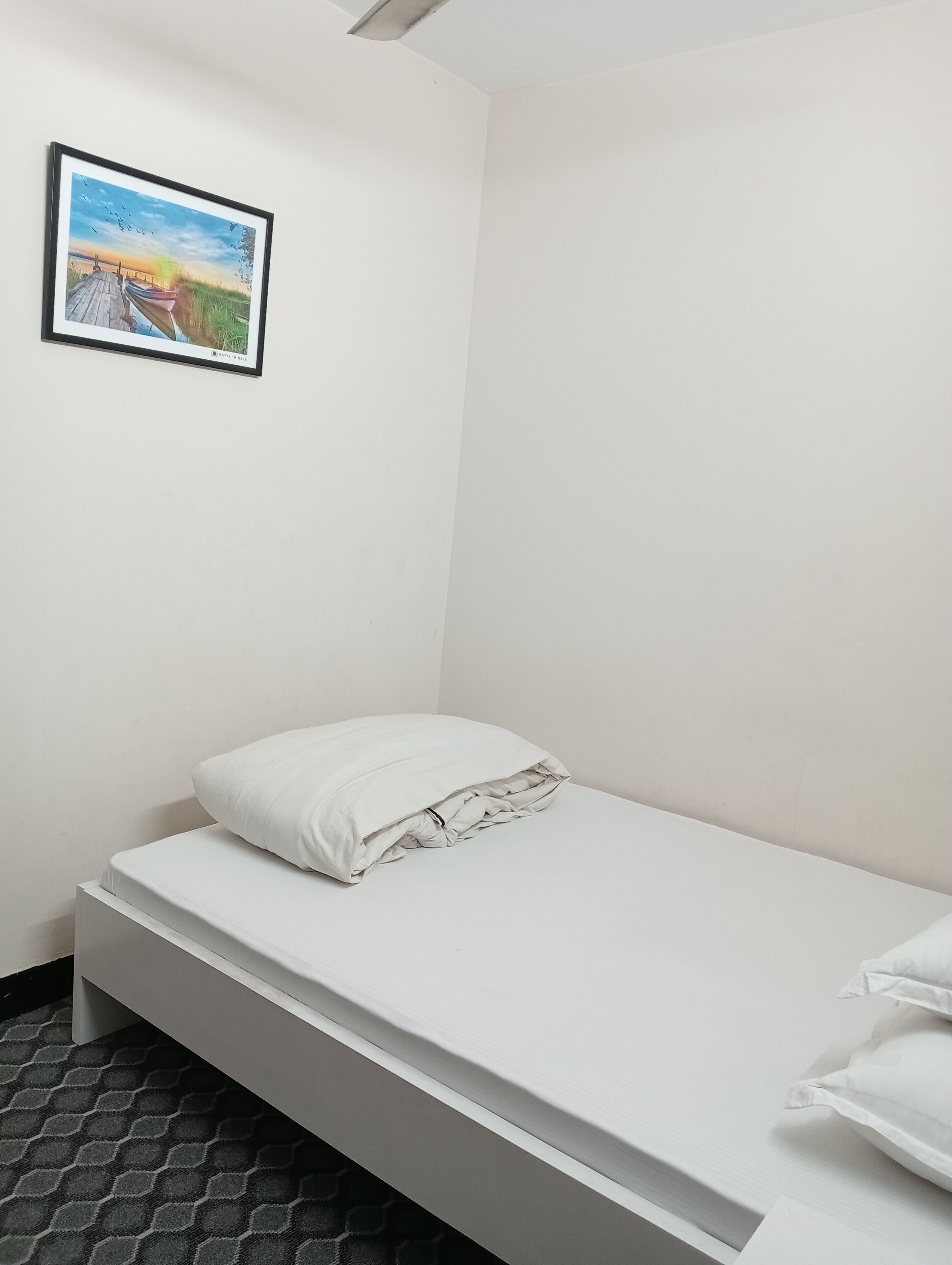 A small, white, single-bed room with a low ceiling and a simple, clean design.