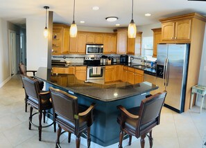 A modern kitchen with wooden cabinets, a central island, bar stools, stainless steel appliances, and pendant lighting. - capri sun (Naples)