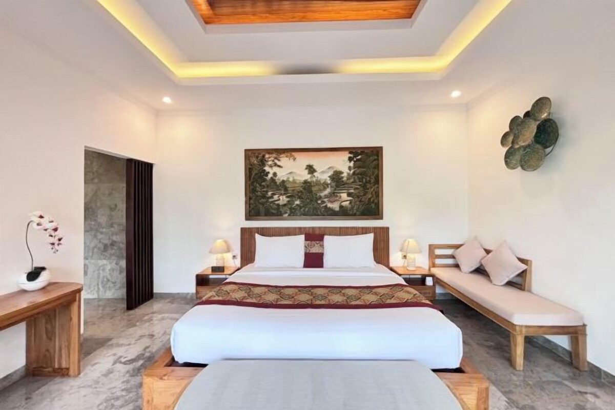 Een moderne slaapkamer met een groot bed, nachtkastjes, een bankje en een schilderij aan de muur.
