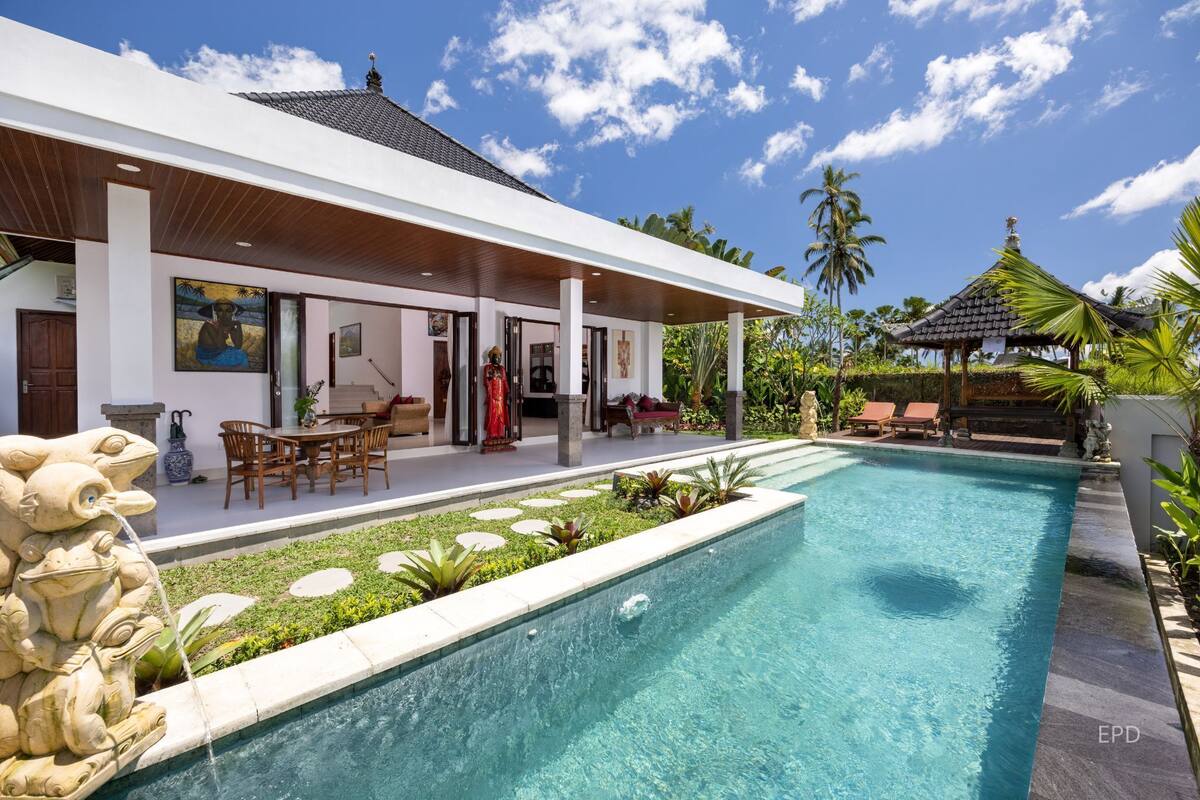 Une maison moderne dotée d’une piscine, de mobilier d’extérieur et de plantes tropicales.