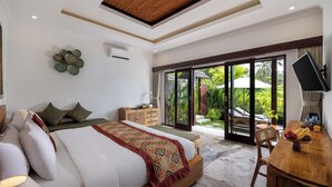 A bedroom with a large bed, a wooden desk, and a sliding glass door leading to a garden. - Arvanya Villa Ubud (Tegallalang)
