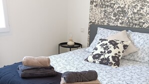 Een opgemaakt bed met een beddegoed met bloemenmotief, een donkerblauwe plaid en drie opgevouwen handdoeken.