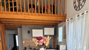 Een moderne keuken met een grote tafel, zwarte stoelen, een witte vaas met bloemen en een houten plafond.