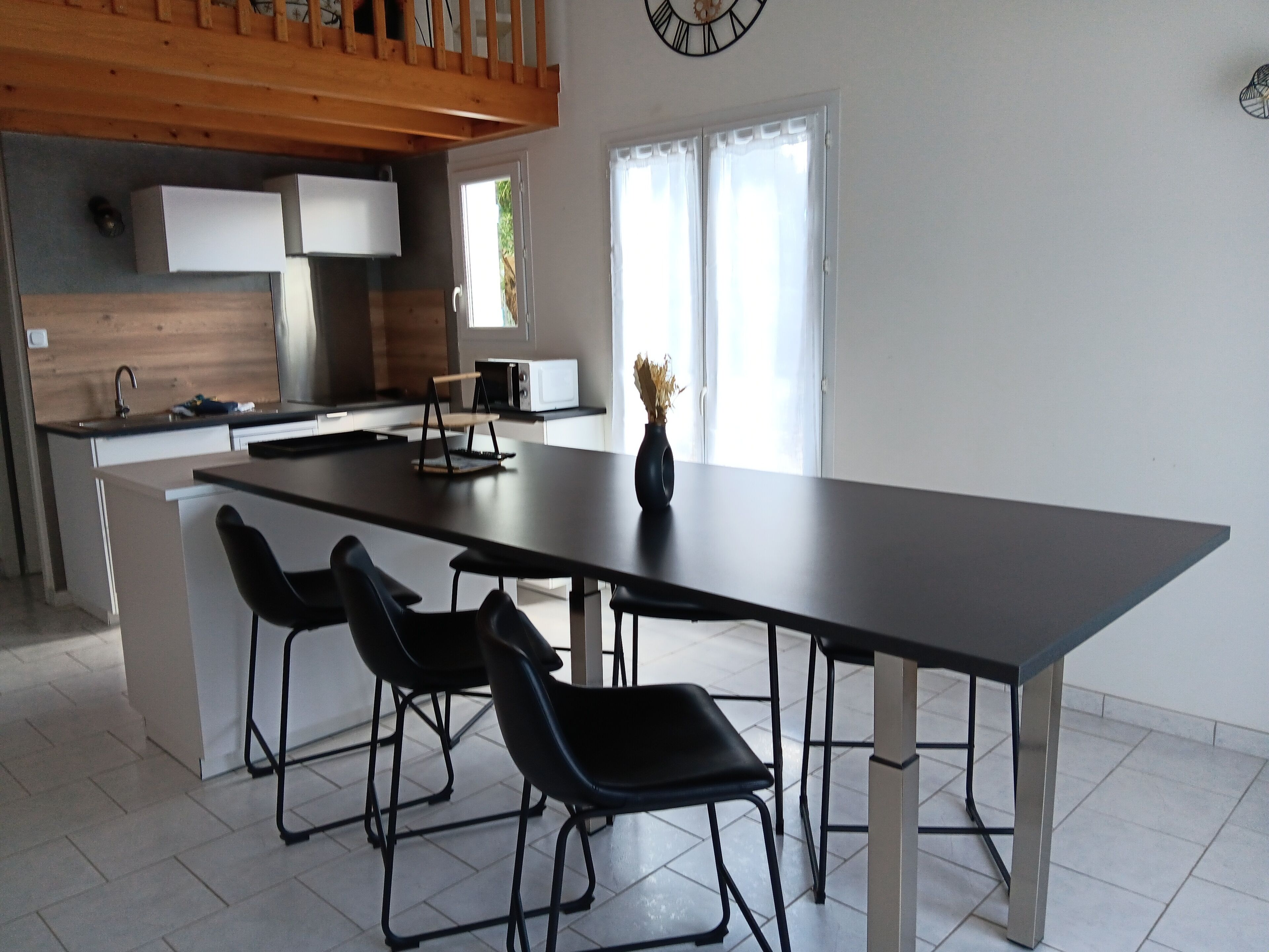 A modern kitchen with a large island, black chairs, and a clock on the wall.