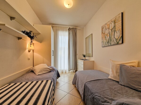 Une chambre d’hôtel avec deux lits, une table de chevet avec une lampe, un miroir, un tableau au mur et une fenêtre avec des rideaux.