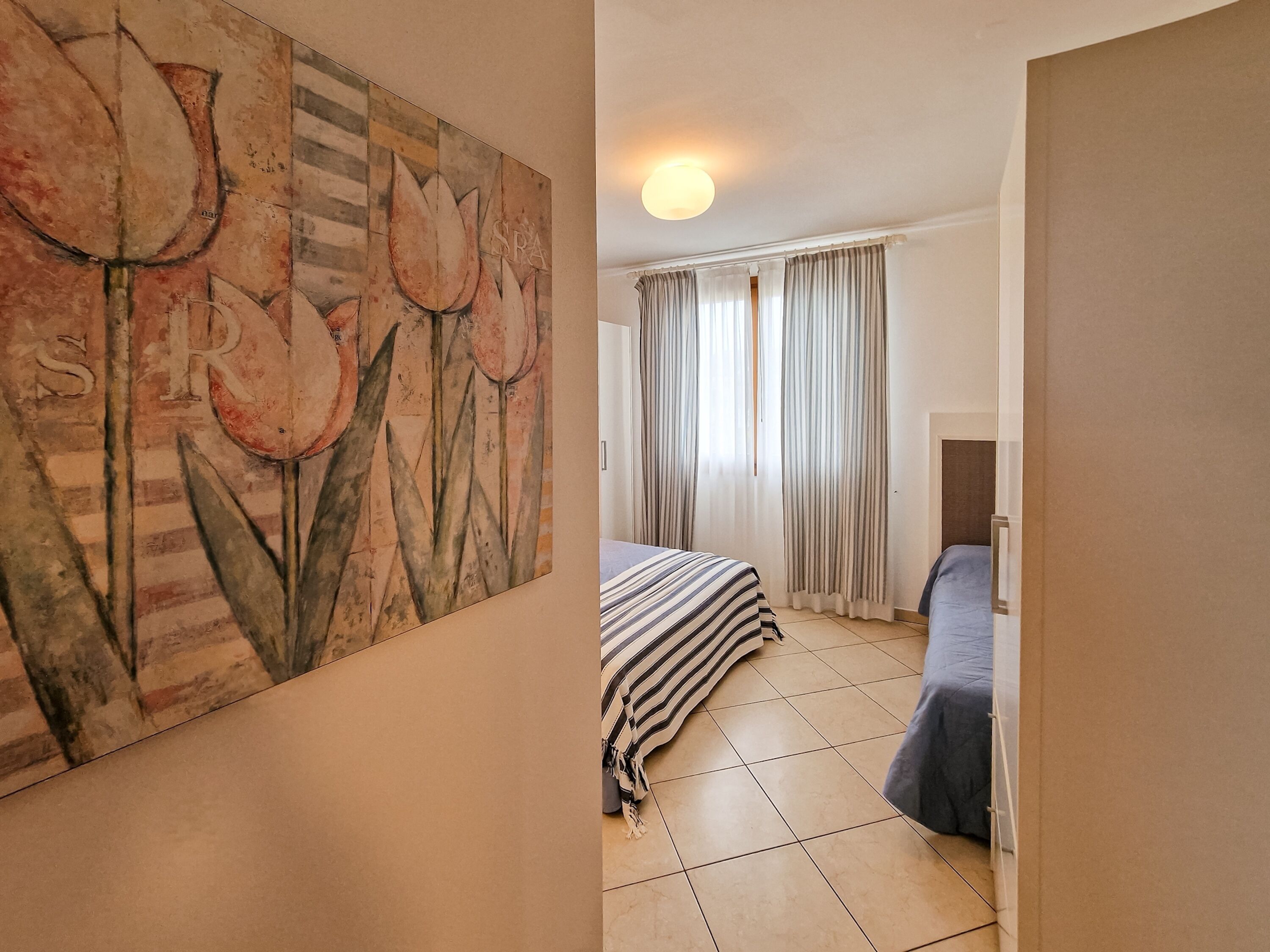 A room with a bed, a painting, curtains, and a door.