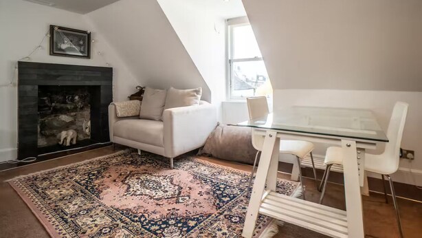 A modern living room with a fireplace, a white sofa, a glass dining table, and a patterned rug.