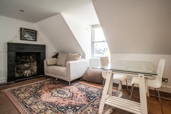 A modern living room with a fireplace, a white sofa, a glass dining table, and a patterned rug.