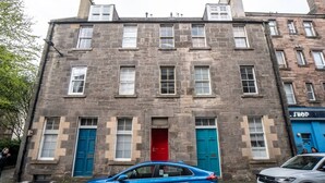 A two-story stone building with a red door, blue doors, and a shop on the right.