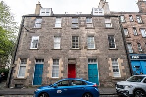 A two-story stone building with a red door, blue doors, and a shop on the right.