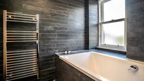 A modern bathroom with a black tiled wall, a glass shower enclosure, and a bathtub.