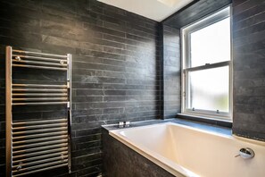 A modern bathroom with a black tiled wall, a glass shower enclosure, and a bathtub.