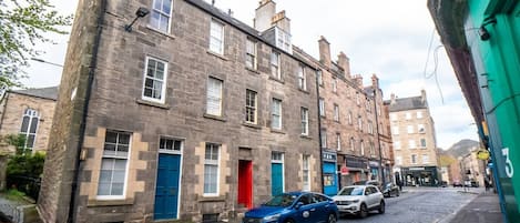 A street with historic stone buildings, a cobblestone road, and parked cars.