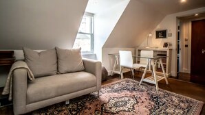 A loft-style room with a sofa, a dining area with chairs, a rug, and a television.