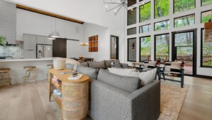 A modern kitchen with white cabinets, a wooden island, and a dining area with a large window overlooking greenery.